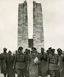 A group of men dressed in Nazi German soldier, front and centre is Adolf Hitler, June 1940. The twin pylons of the memorial are clearly displayed in the background.