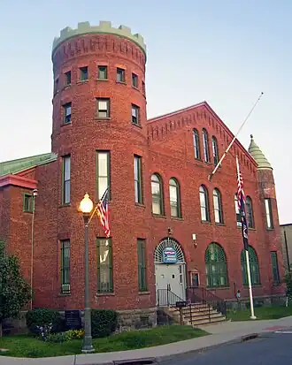 A brick building with a castle-type tower on the left and a smaller tower with green roof on the right