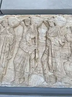 Three young men holding "hydriai" (water jugs), part of the Panathenaic procession depicted in the Parthenon frieze.
