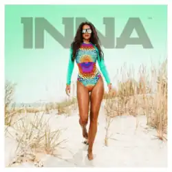 Photograph of Inna posing in a colorful bathing suit while at a beach.