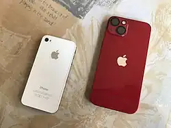 A (PRODUCT)RED iPhone 13 alongside a white iPhone 4s released a decade ago. Showing the back side view. Note the camera protector installed on the iPhone 13.
