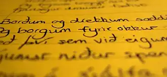 Photo of black handwritten text on a seemingly yellow paper with the top and bottom blurry and vertical middle clear