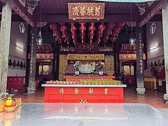 The inner sanctuary of Kuan Im Teng, adorned with red lanterns and central offering tables. The hall enshrines Guanyin and other deities.