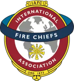 A white and gray globe surrounded by a red circle reading "International Association," with a blue band running horizontally across the circle reading "Fire Chiefs"