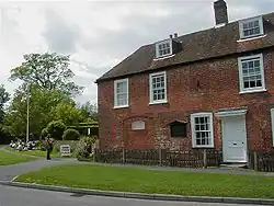 Photograph of a two-story brick house with dormer windows emerging from the roof to suggest a small third story.