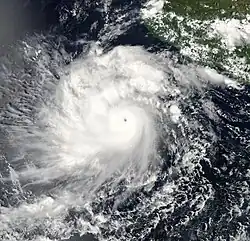 A photograph of a powerful hurricane off the Pacific coast of Mexico. It has a small and clear eye surrounded by a thick ring of solid white clouds, indicating intense convection. There are several well-pronounced rainbands, especially on the left side of the hurricane. Also on the left side of, and perpendicular to, the hurricane are some thin streaks of high clouds jutting out westward; these are indicative that the hurricane has healthy outflow, which is one of the things a tropical cyclone needs to get stronger and stay strong.