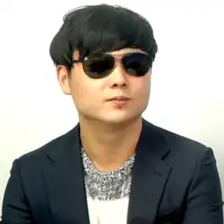 A portrait photograph of Jeong Haneul. He is wearing a pair of aviator sunglasses and has short, black hair.