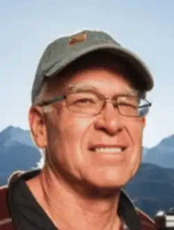 small headshot of Fielder an older white man in glasses wearing a ballcap with a mountain backdrop