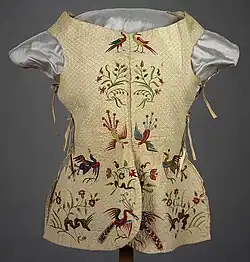 A garment resembling a quilted vest with ties at the sides. It is decorated with red and green embroidered birds and flowers.