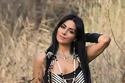 Kelly Derrickson in traditional costume standing in the tall grasslands on Okanagan territory