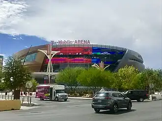 A gold and grey sports arena with trees and cars in front of it.