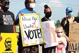 Protesters along funeral procession wearing COVID mass and holding signs