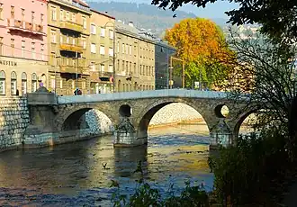 Latin bridge (prev. Princip bridge) in Sarajevo. Across the bridge is a street of several grayish houses not more than four stories high.