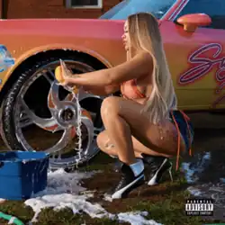Latto squatting in high heels and apple bottoms shorts, carwashing a brightly colored lowrider.
