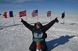 A man posing at the indication of the South Pole, with flags of the countries that have visited it