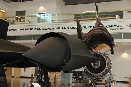 Entry to the inlet. Behind is the outer wing and hinged portion of the nacelle that encloses the engine. The spike is shown in the forward position (for speeds below Mach 1.6). Just discernible behind the cowl lip are spike boundary layer bleed slots where the normal shock is located at higher speeds when the spike has moved rearwards, the cowl bleed "shock trap" ram intake, streamlined bodies ("mice") and, between the mice, the forward bypass door openings[75] that dump unwanted air externally through the front louvers and cause nacelle drag.[76] When the landing gear is down, ambient air flows in reverse through the bypass to supplement the front inlet flow into the engine.