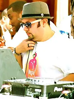 A man wearing a white T-shirt and bowler hat at a mixing table