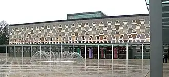 Panoramic shot of the Grand Théâtre de Luxembourg, a modernist-style building, with a pavement fountain in front