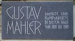 A dark plaque with white lettering in which the composer's name is shown in extra large characters on the left, the main message in smaller characters on the right