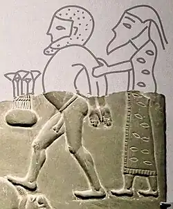 Man in patterned and fringed dress (probably a Lybian),[10] behind naked prisoner.[11][6]