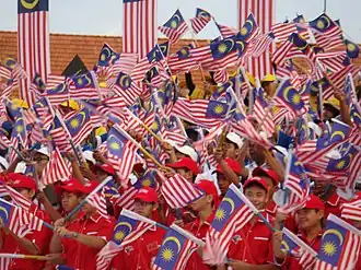 A large crowd of boys in red shirts and caps waving Malaysian flags