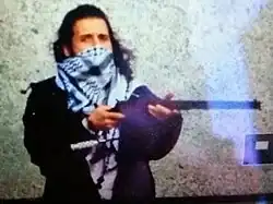 low resolution photo of the shooter holding a hunting rifle with their face partially obscured by a scarf on the day of the attack