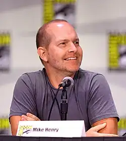 A man with close-shaven hair, and a slight beard, looks to his left, with his body turned.