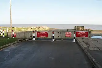 Concreter blocks across a tarmacked road, with a sheer drop and sea beyond