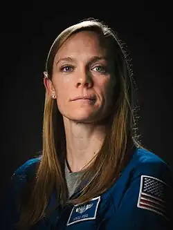 A woman in a blue flight suit; she is facing the camera and smiling.