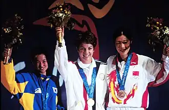 Three women sporting Olympic medals around their necks, with one holding a bouquet, celebrating their individual Olympic achievements together.
