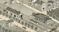A detail from a bird's eye view map. It shows two one-story buildings along a rail line in a village center.
