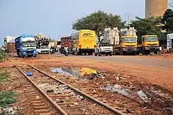 A railroad track in poor condition, in front of a busy highway with cars, buses, and motorcycles.