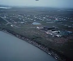 An aerial view of Nuiqsut, showing lines of structures evenly spaced and laid out in a rectangle along the shore of a river