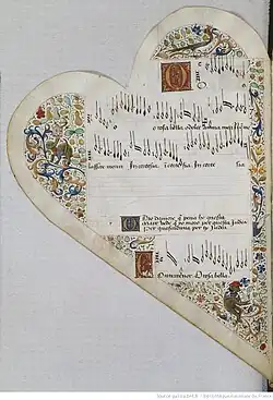 Medieval manuscript leaf shaped like a heart. It bears 5 musical staves: the 3rd is empty, the 4th is filled with lyrics, the rest are filled with musical notation in black ink with lyrics below. The lyrics open with enlarged initials in gold on painted squares. Surrounding the staves are decorative borders in gold and colours consisting of blocks of curling vines from which spring leaves and flowers. Cavorting among the foliage are a large bird, a monkey wearing a red hat while reading a book, and a 4-legged monster with a snake-like neck and the face of a lion.
