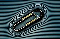 A metal paperclip floating on water. A grille in front of the light has created the 'contour lines' which show the deformation in the water surface caused by the metal paper clip.