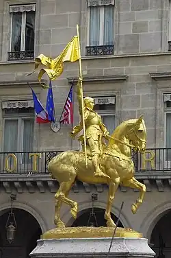 Gold statue of Joan of Arc holding flag and riding horse