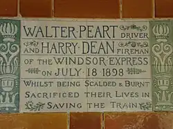 A tablet formed of two large tiles, bordered by green flowers in the style of the Arts and Crafts movement