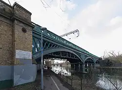 A viaduct crossing a river with three arches, viewed from almost underneath it on one side of the river. A plaque is visible on the abutment of the bridge