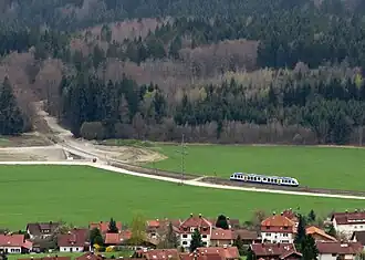 White-and-blue train crossing a green field and preparing to ascend a hill