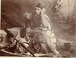 A sepia-toned portrait of a bearded man in Ethiopian costume, including a headwrap, seated with an ornate shield.