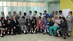 Color image of President Piñera visiting the rescued miners, who are dressed in hospital robes and pajamas while seated and standing in a semi-circle in a hospital room