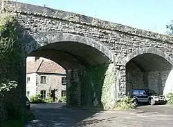 Two arches of a stone and brick bridge with a car beneath.