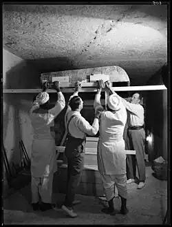 Four men lifting large wooden beams that support a decorated lid