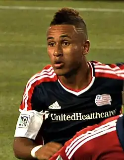 A soccer player in a New England Revolution jersey is running.