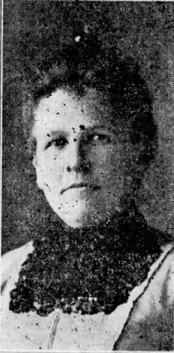 B&W portrait photo of a middle-aged woman with her hair in an up-do wearing a frilly, dark blouse