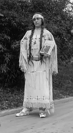 Ruth Muskrat, holding The Red Man In The United States (1919), by Gustavus Elmer Emmanuel Lindquist (1886-1967), on December 13, 1923. The book's beaded cover and dress were made by an Indian woman of the Cheyenne tribe, Fish Woman. The book is an study of the social, religious, and economic life of American Indians, made under the auspices of the Institute of Social and Religious Research.