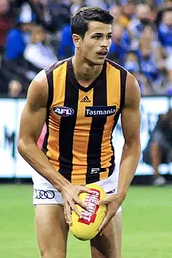 Male athlete in sleeveless guernsey holds football