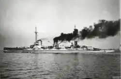 A large ship steams at full speed: the ship plows into the sea while dark gray smoke pours from its smoke stacks.