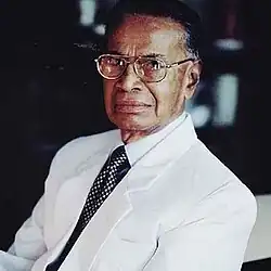 Sam Wijesinha sitting on a chair, slightly facing left.