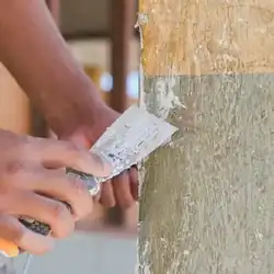 White spackle is applied to a painted surface using a small putty knife.